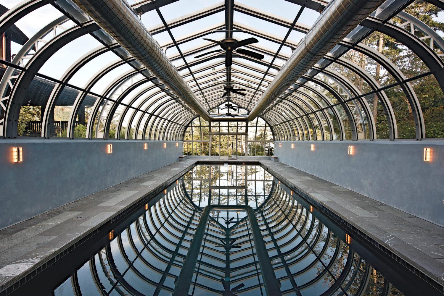 Бассейн внутри остеклённого павильона-оранжереи под стеклянной кровлей с видом на сад за стеклом в Сыктывкаре